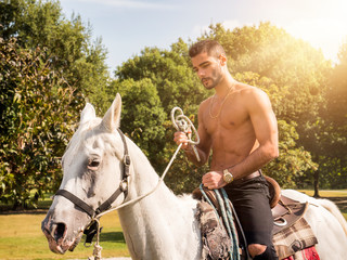 Handsome muscular man without shirt riding horse in natural bright sunlight.