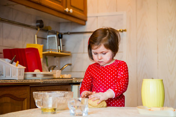 a cute little girl with blue eyes and red clothes is making cakes out of flour in the kitchen at home during the quarantine