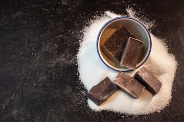 A bowl of chunks of bakers chocolate sitting on a pile of white sugar cane  