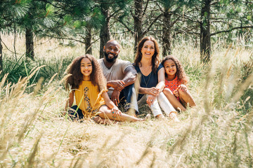 Portrait of happy mixed race family sitting in grass in park in summer