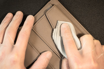 Male hands in disposable gloves erase fingerprints from an opened wallet on a black background. Gloved hands disinfect the wallet.