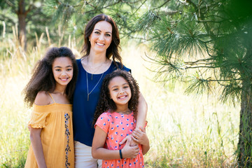 Portrait of mom hugging her daughters outside in summer