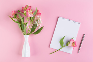 Alstroemeria and gypsophila flowers in a white vaseand blank white paper and pen on a pink...