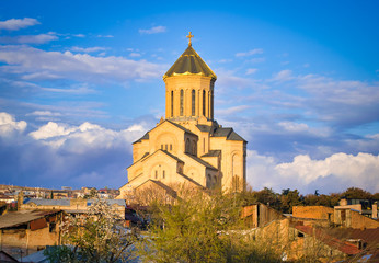 Fototapeta na wymiar Orthdodox holy trinity church in Tbilisi with many hosues around and blooming spring trees. Religion and culture of Kartvelians. Sakartvelo.