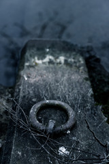 Rusty mooring ring for boats and ships on a stone that protrudes into the water; depressive
