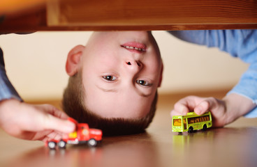 portrait of a child of a preschool boy upside down with a toy car and a bus in his hands. View from...