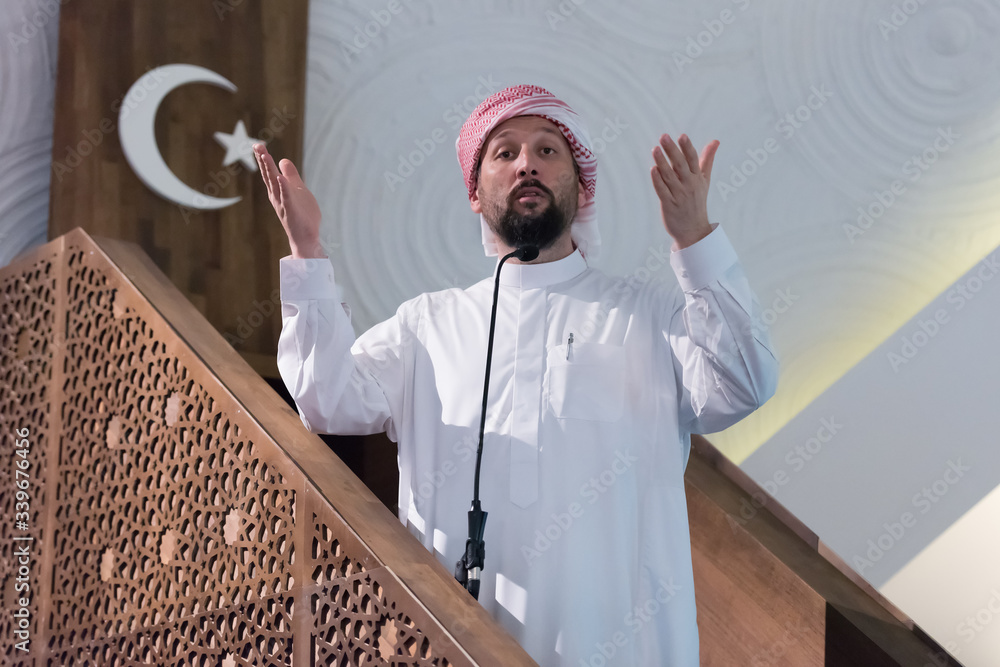 Wall mural Muslims young arabic Imam has a speech on friday afternoon prayer in mosque. Muslims have gathered for the friday afternoon prayer in mosque and are listening to the speech of imam