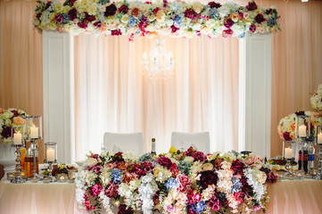 Festive table, arch, stands decorated with composition of pink, white, purple flowers and greenery, candles in the banquet hall. Table newlyweds in the banquet area on wedding party.