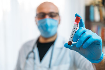 Doctor Holding Pandemic Coronavirus 2019-nCoV Blood Sample Positive Test Tube. Doctor wearing medical mask and gloves and shows patient's blood test tube containing corona virus (COVID-19)