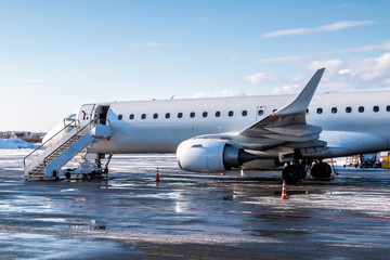 White passenger jet plane with air-stairs at the cold winter airport apron