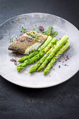 Fried gourmet skrei cod fish filet with green asparagus and lettuce offered as closeup on a modern design plate with copy space