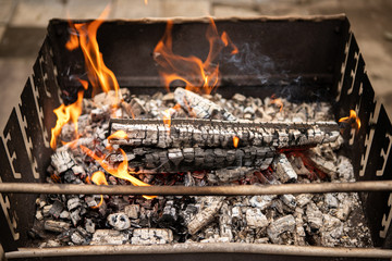 Flaming log (wood) in a metal outdoor brazier with ashes and smoke in rural courtyard