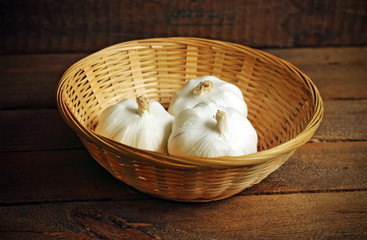 Three garlics in wicker basket on wood