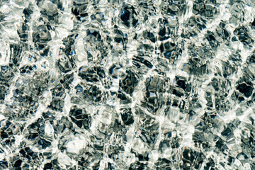 Abstract background of crystal clear sea water. Black and white pebbles under transparent water surface. Water pebbles pattern