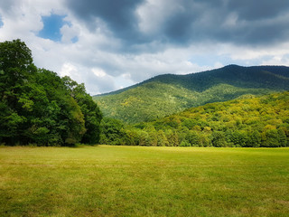 Green field, forest with a mountain in the background and thunderclouds. Adygea, Caucasian Nature Reserve