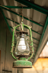 Green rustic retro  petroleum lamp 
hanging from the roof in a courtyard