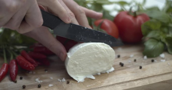 Tagliare mozzarella di bufala su un tagliere per preparare una caprese, ricetta italiana