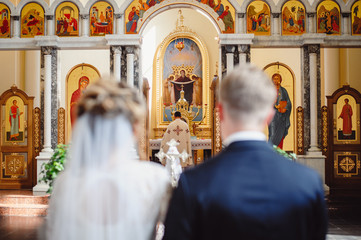 Newlyweds at the wedding ceremony in the church are facing the altar. The priest blesses the bride...