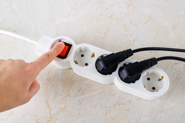 Woman hand going to push power button on a white extension cord with four outlets. Electric power strip with  switch for home or office.