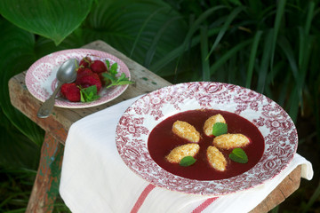 Cottage cheese gnocchi with strawberry sauce and lemon balm leaves on the background of the summer garden. Rustic style.