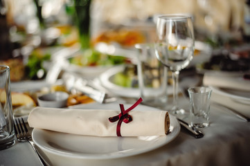 Serving, setting table. plates and silverware cutlery linen napkin are decorated with red ribbons . Close up. Banquet hall in the restaurant. Concept: Serving. Celebration. Anniversary. Wedding