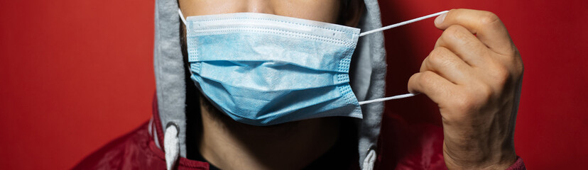 Close-up of male face with hoodie, put on medical safety respiratory mask against coronavirus on red background.