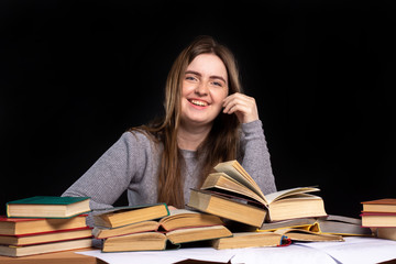 girl sitting at a table with open books with a smile. Black background. isolate. student preparing for exams. distance learning