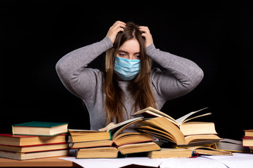 a young girl in a medical mask sits against a black wall behind stacks of books. self-education