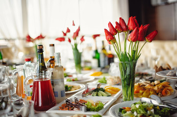 Served in a restaurant. Snacks, salads and a bunch of flowers of red tulips at the banquet table at the restaurant. Beautifully served banquet table with flowers and candles
