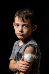 Cute little boy with sticking plaster on arm on black background