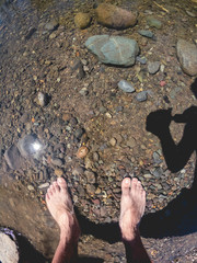 Man feet on shallow river with rocks on sunny day, Cajón del Maipo, Chile