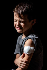 Cute little boy with sticking plaster on arm on black background