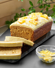 Vegan orange loaf cake and  slices.Homemade citrus cake with white cashew cream on top. Green spring leaves around.