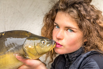 The kiss - Young beautiful woman with curly hair kisses a carp