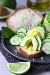 Healthy vegetarian sandwich with no knead homemade bread, avocado and cucumbers for breakfast or lunch. Light grey stone background. 