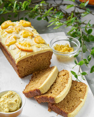 Vegan orange loaf cake and  slices.Homemade citrus cake with white cashew cream on top. Green spring leaves around.
