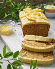 Vegan orange loaf cake and  slices.Homemade citrus cake with white cashew cream on top. Green spring leaves around.