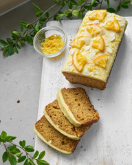 Vegan orange loaf cake and  slices.Homemade citrus cake with white cashew cream on top. Green spring leaves around.