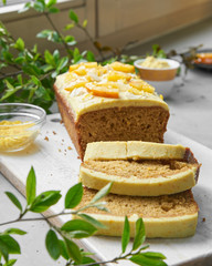 Vegan orange loaf cake and  slices.Homemade citrus cake with white cashew cream on top. Green spring leaves around.