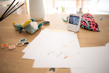 Home work with paint colors, toys and baby camera guard on a wooden table on a domestic scene during quarantine