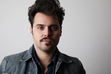 Headshot of serious stylish man looks straight with confident expression, wears denim jacket, isolated.