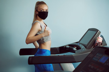 A pretty girl in a protective mask is engaged on a cardio simulator.Protective masks against virus infection. Training during quarantine in the gym. Coronavirus (COVID-19) protection concept