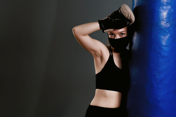 Young girl in a protective mask stands near a punching bag. Protective masks against virus infection. Training during quarantine in the gym. Coronavirus (COVID-19) protection concept.