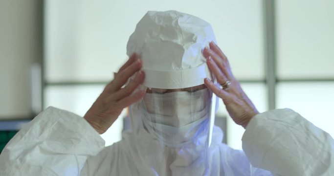Portrait of a tired solemn mature female doctor in full PPE who removes her protective garb at the end of a long shift of working with COVID19 infected patients.