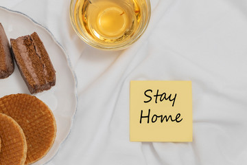 Stay home phrase on cozy home background with cup of tea and sweets. Self-isolation motivation during COVID-19 outbreak concept