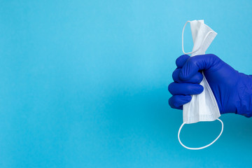 Protective face mask or medical mask in hand protected by blue gloves on blue background. Coronavirus disease. Concept of health and medicine, virus prevention.