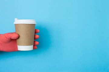 Coffee cup in hand with protective gloves isolated on blue background. Hand with paper cup. Mockup of female hand holding a coffee paper cup. Copy space, coronavirus protection