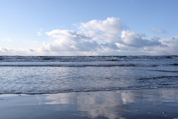 Fototapeta premium The Baltic Sea coast in winter, the sun shines and there are clouds in the sky, but the sea has waves that form a beautiful reflection in the water