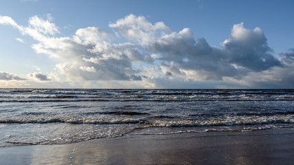 The Baltic Sea coast in winter, the sun shines brightly and there are clouds in the sky, but there are waves in the sea