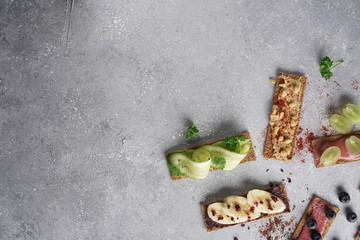 Healthy vegan sandwiches with hummus, guacamole, chocolate, cream, berries and raw spring vegetables on crispy rye bread. Flat lay on a gray background. Free empty space